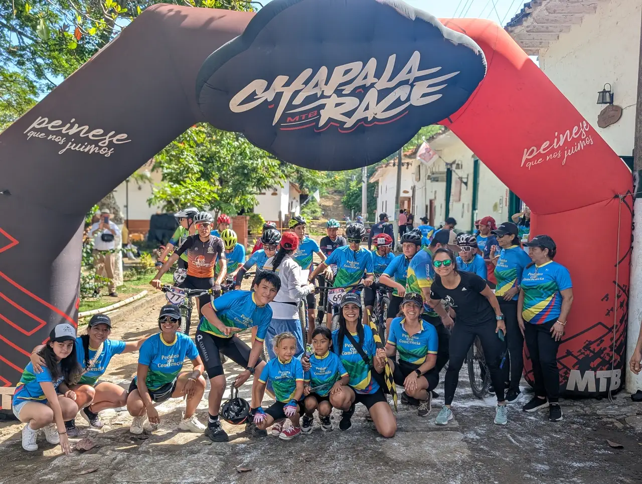 Participantes de Pedalea con Conciencia reunidos bajo un arco de un evento de ciclismo