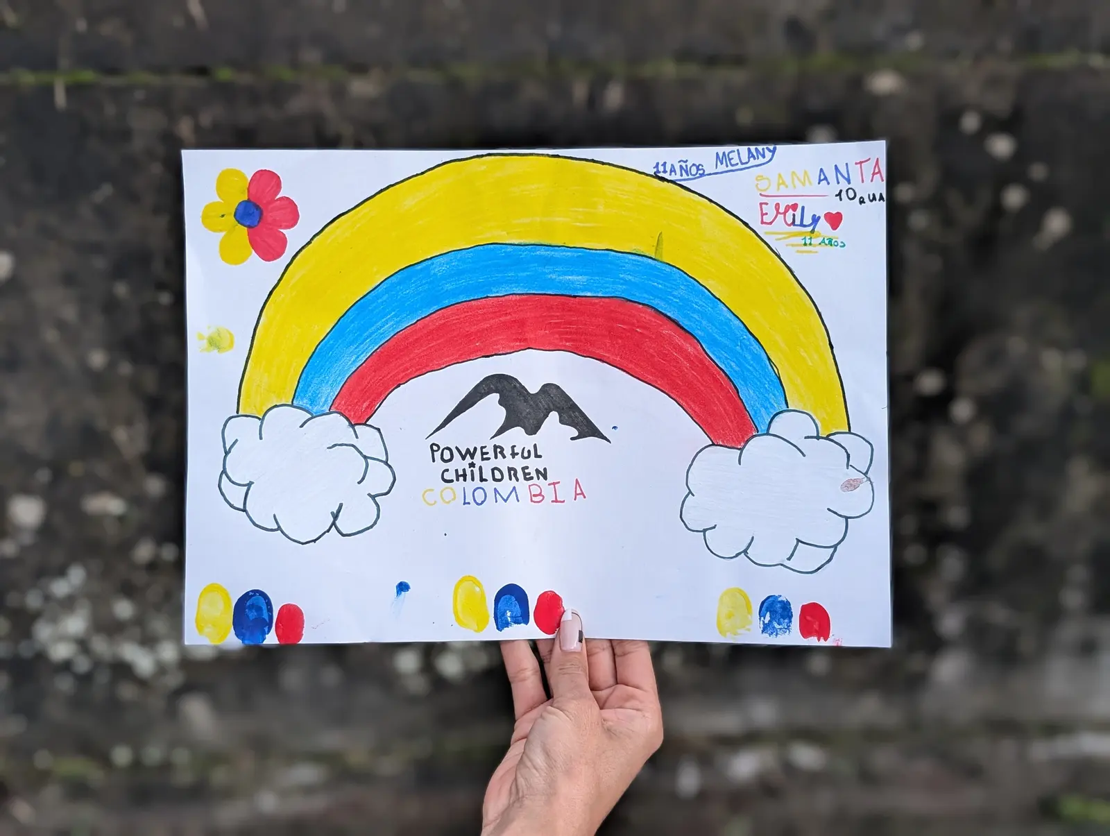 Dibujo de un niño con los colores de la bandera de Colombia, montañas, nubes, flores y el logo de Powerful Children Colombia